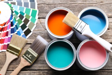 Cans of bright paints, brushes and color palettes on wooden table, flat lay