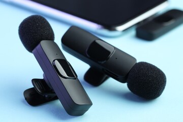 Lavalier microphones and smartphone with wireless receiver on light blue background, closeup