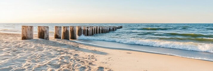 Serene beach scene with gentle waves lapping the shore, meeting a line of weathered wooden posts.  Sandy beach stretches to the foreground