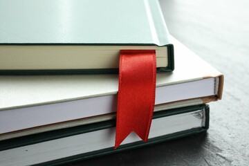 Book with red ribbon bookmark and colorful ones on grey textured table, closeup
