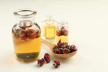 Open perfume bottles with aromatic essential oils and dried roses on white table, closeup. Space for text