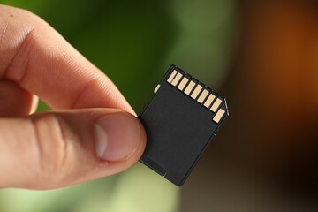 Man with SD memory card on blurred background, closeup