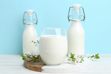 Fresh milk and blossoms on white table against light blue background