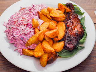 Simple meal with pork belly, potato wedges and pink coleslaw on white plate. Fine dinner with simple products.