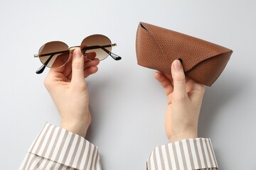 Woman with sunglasses and case on light grey background, top view