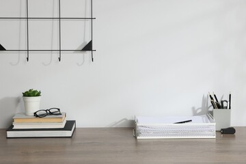 Naklejka premium Different stationery, floral decor and glasses on wooden office table near white wall