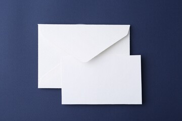 Blank greeting card and paper envelope on dark blue background, top view
