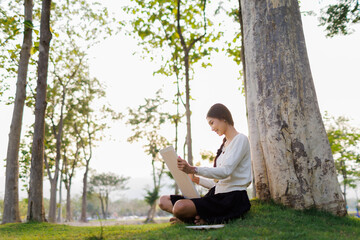 Bathed in warm golden light beneath a tree, a smiling female student immerses herself in her...