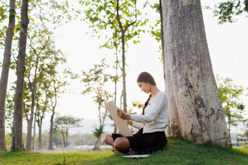 Bathed in warm golden light beneath a tree, a smiling female student immerses herself in her...