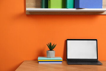 Stylish workplace with modern laptop on wooden desk near orange wall. Space for text