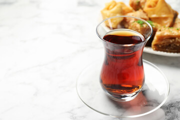 Tasty Turkish tea served with baklava on white marble table, closeup. Space for text