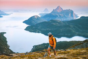 Man backpacker hiking solo in mountains of Norway travel climbing adventure outdoor, healthy lifestyle summer vacations tour active traveler roam alone enjoying sunset islands and sea landscape