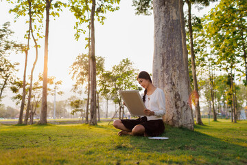 Bathed in warm golden light beneath a tree, a smiling female student immerses herself in her...