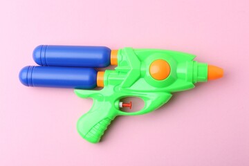 Bright plastic water gun on light pink background, top view