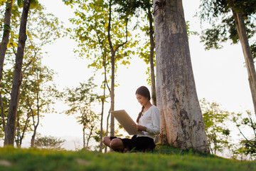 Bathed in warm golden light beneath a tree, a smiling female student immerses herself in her...