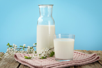 Fresh milk and blossoms on wooden table against light blue background, closeup