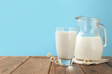 Fresh milk and flowers on wooden table against light blue background, closeup. Space for text