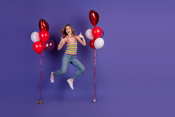 Happy young woman jumping in casual outfit with colorful balloons on a purple background