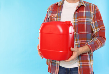 Fototapeta premium Man holding plastic canister on light blue background, closeup. Space for text