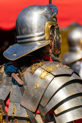 close view of a roman military helmet and shoulder armor, segmented roman armor and red tunic