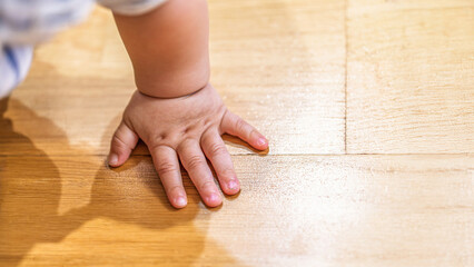 Small baby hand pressing on polished wooden floor close-up, concept of childhood and innocence