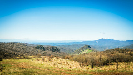 Naklejka premium Serene spring landscape in Kakheti, Georgia, featuring forested hills, lush green meadows, and distant snow-capped peaks under a clear blue sky