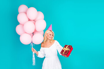 Smiling blonde woman holding pink balloons and gift box against teal background celebrating occasion with charm and style