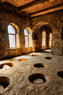 Traditional Georgian wine cellar with sunlit arched windows and underground clay vessels (qvevri) embedded in the stone floor. Historic winemaking architecture in the Kakheti region