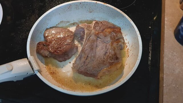 Delicious looking steak searing in a white pan ontop of a black stove