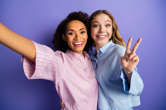 Young female friends taking a cheerful selfie against a purple background while celebrating together in stylish and casual outfits.