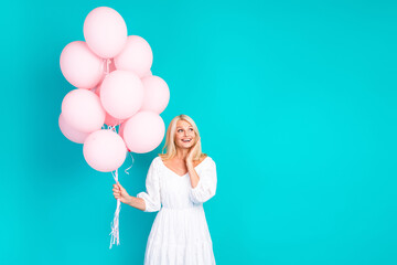 Joyful blonde woman holding pink balloons against a turquoise background in a white dress, showcasing happiness, charm, and lifestyle