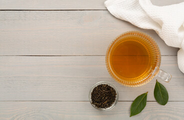 Cup of tea with dry and fresh leaves on wooden background, top view