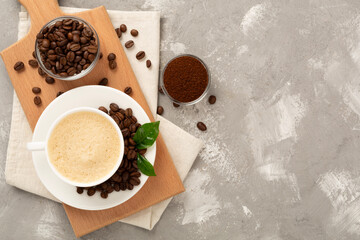 Cup of coffee with coffee beans and leaves on concrete background,top view