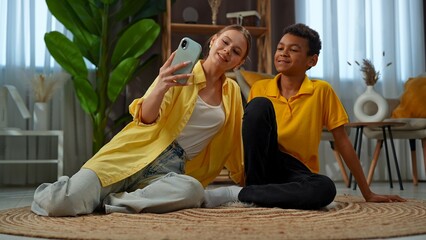 Young african american child boy spending free time at home, kid with mom on the floor in the living room taking selfies together on smartphone.