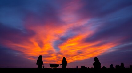 Three people silhouetted against a vibrant sunset sky, grilling food on a rooftop overlooking a city skyline