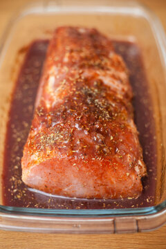 Close-up of a Raw pork tenderloin in a glass dish marinating in a marinade with herbs