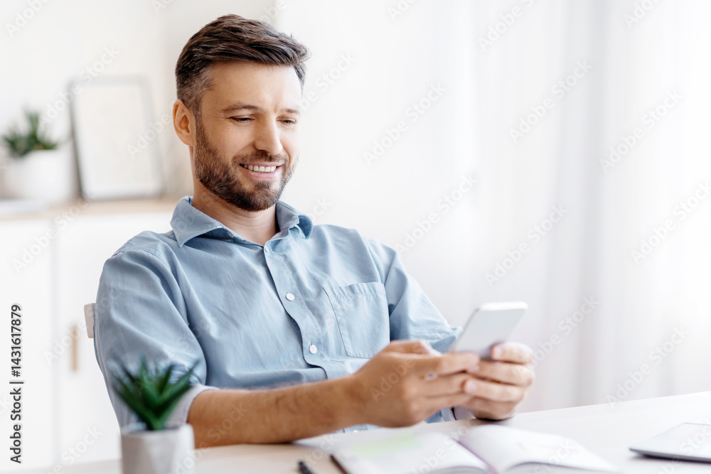 Poster handsome young businessman using smartphone at workplace in office, checking new application, browsi