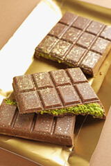 Pieces of delicious Dubai chocolate with pistachios and knafeh on dark beige background, closeup