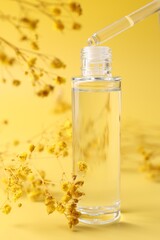 Dripping serum from pipette into bottle and gypsophila flowers on yellow background, closeup