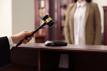 Judge striking gavel at wooden table in courtroom, closeup
