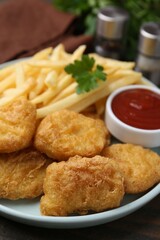 Tasty chicken nuggets and french fries with sauce on wooden table, closeup