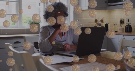 Image of coins over senior african american woman paying bills on laptop