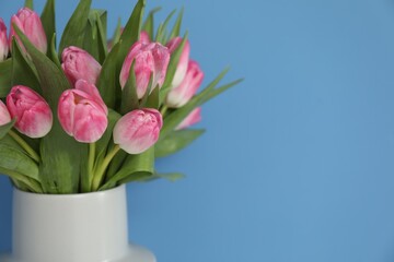 Bouquet of beautiful tulips in vase on light blue background, closeup. Space for text