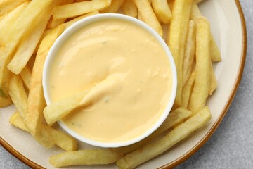 Tasty cheese sauce in bowl and French fries on grey table, top view