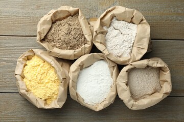 Different types of flour in paper bags on wooden table, flat lay