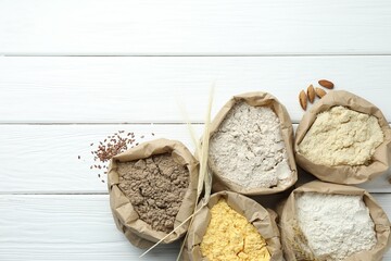 Different types of flour in paper bags on white wooden table, flat lay. Space for text