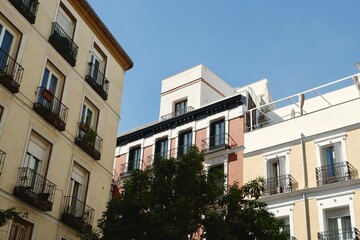 Colorful buildings with wrought iron balconies rise against a bright blue sky in a picturesque street in Madrid, Spain