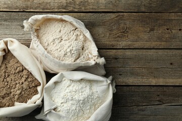 Different types of flour in bags on wooden table, flat lay. Space for text