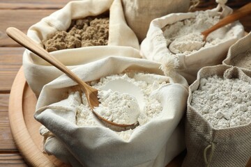 Different types of flour in bags on wooden table, closeup