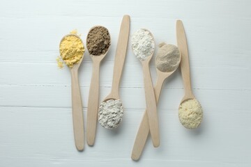 Different types of flour in spoons on white wooden table, flat lay